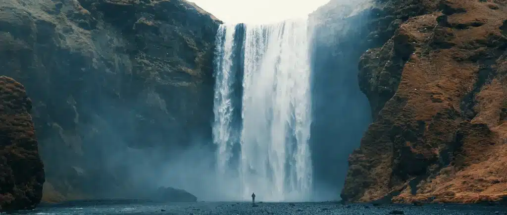 Eine einzelne Person steht am Fuß eines sehr hohen Wasserfalls.